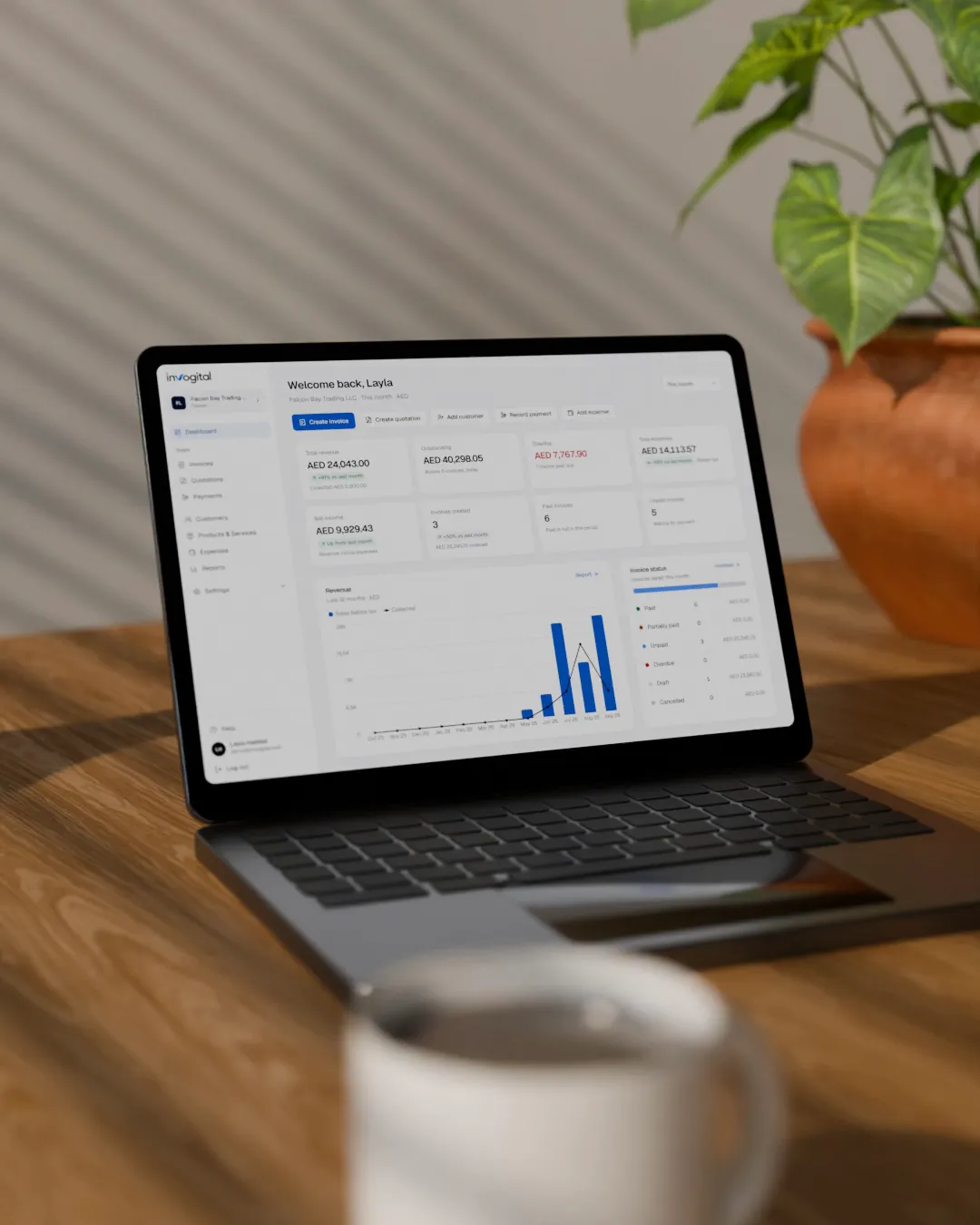 The Invogital dashboard open on a laptop on a wooden desk, beside a plant and a coffee cup